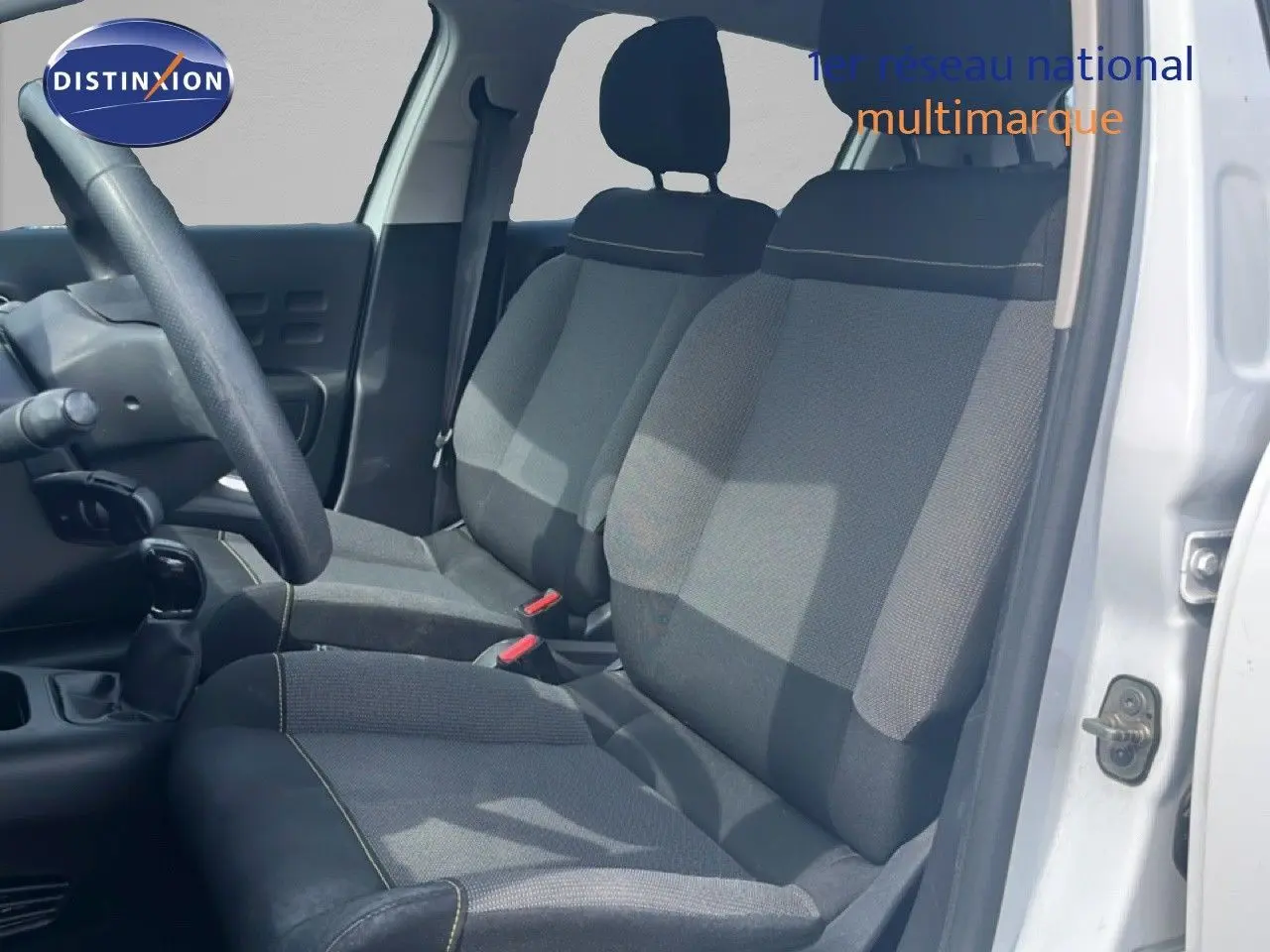 Vue intérieure côté conducteur d'une Citroën C3 blanche 2018, sièges en tissu gris avec coutures contrastantes.