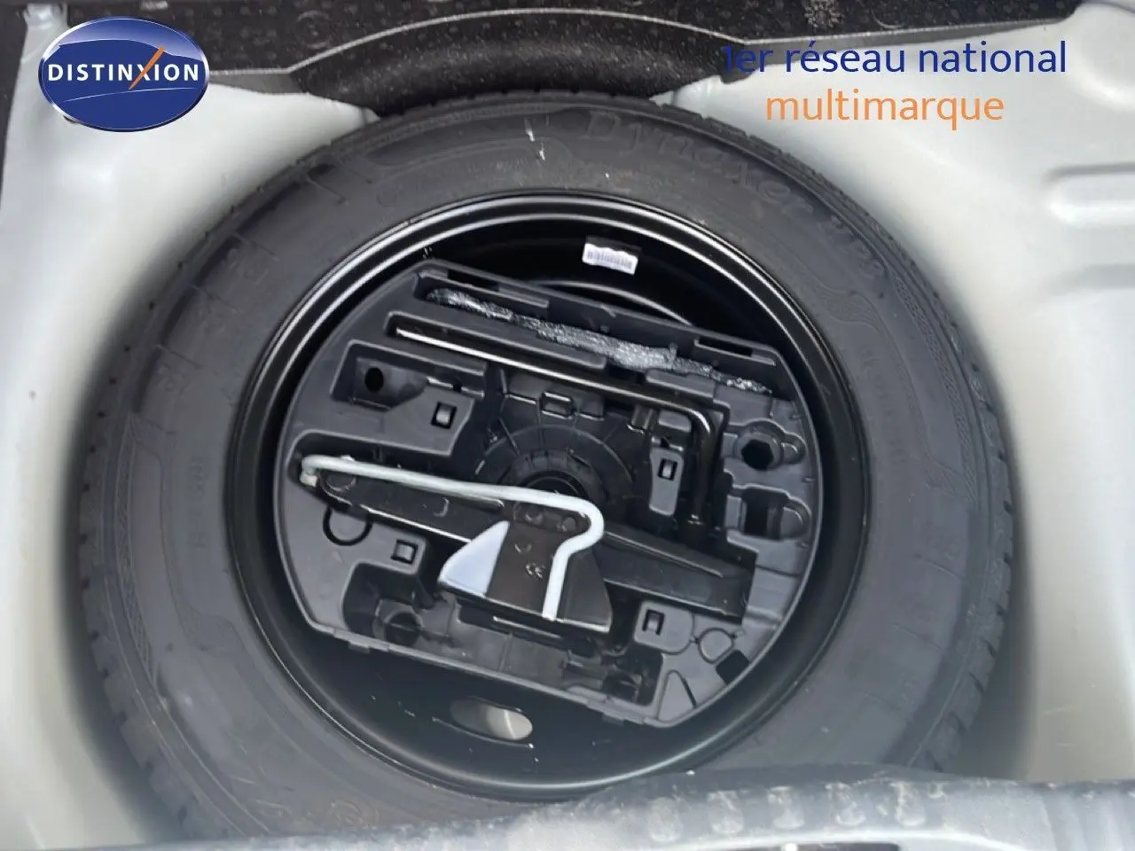 Gros plan sur la roue de secours noire et ses outils dans le coffre d'une Citroën C3 blanche de 2018.