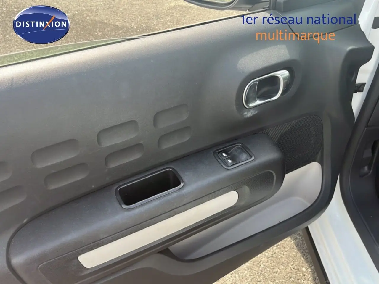 Vue rapprochée de la porte avant droite blanche d'une Citroën C3 2018, avec commande de fenêtre électrique et poignée chrome.