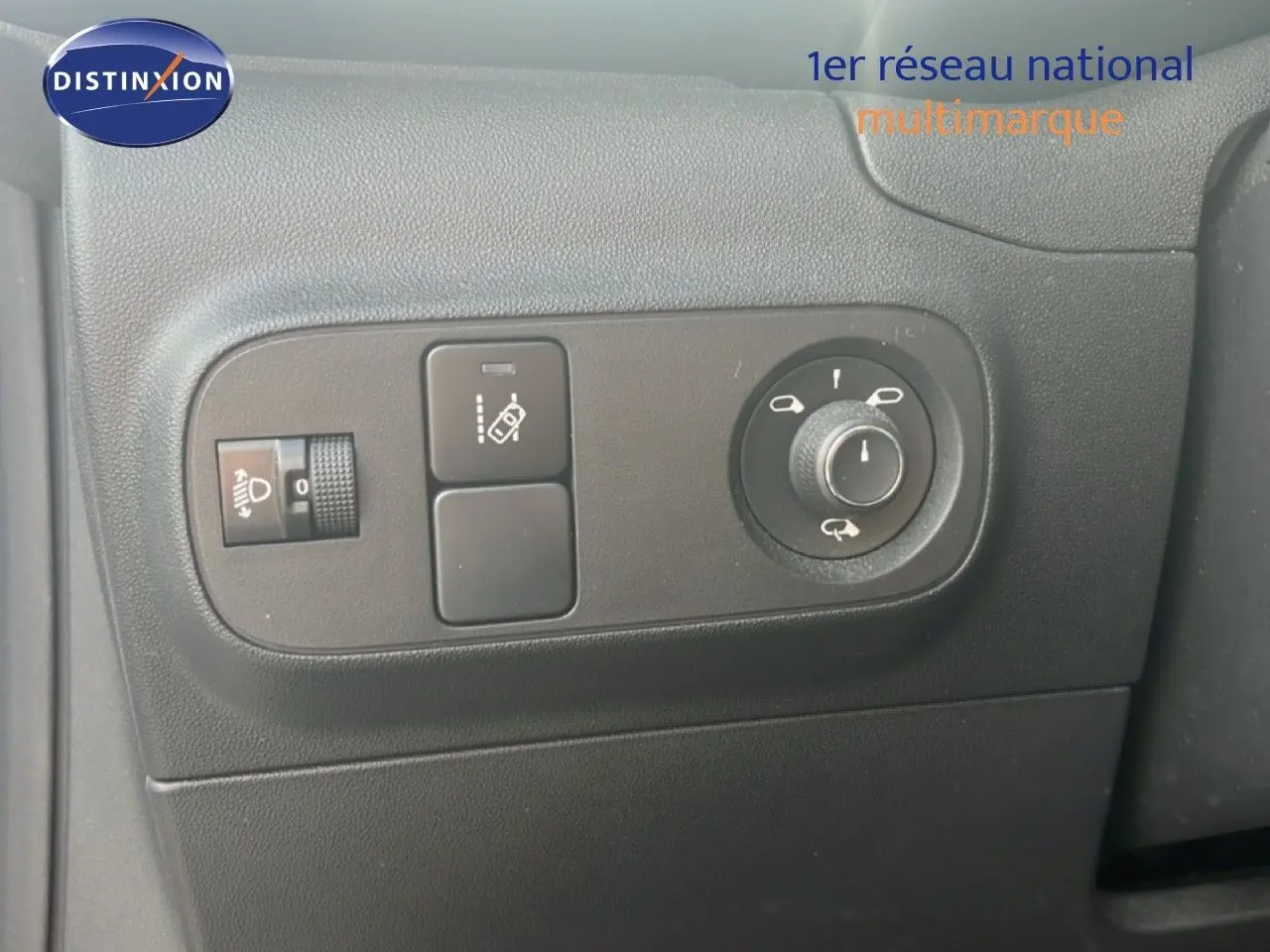 Gros plan sur les commandes de réglage des rétroviseurs et des phares à gauche du tableau de bord d'une Citroën C3 blanche.
