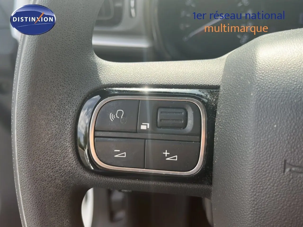 Gros plan sur les commandes de volume et téléphone intégrées au volant noir d'une Citroën C3 blanche de 2018.