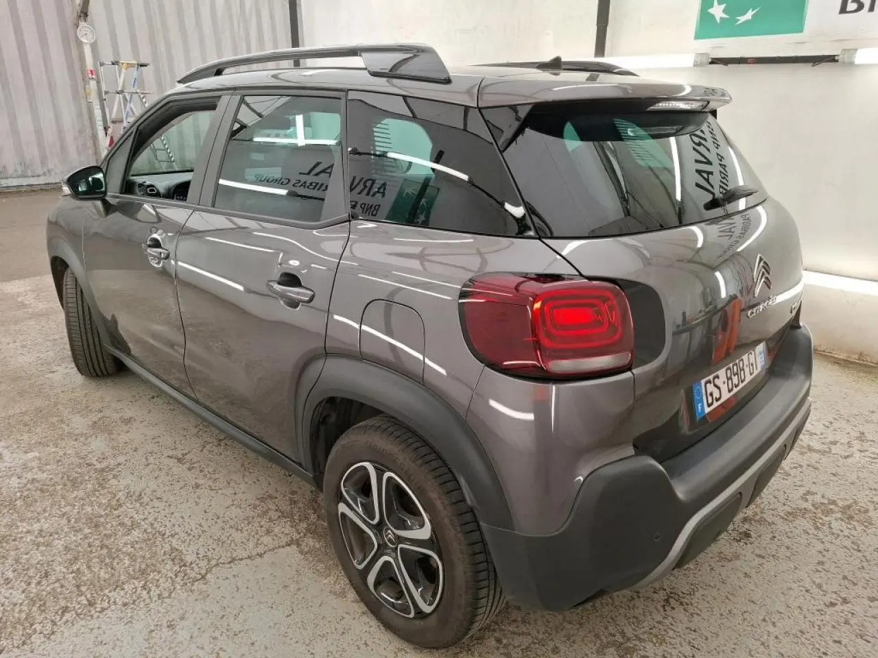 Vue 3/4 arrière droite d'un Citroën C3 Aircross gris foncé avec barres de toit noir brillant et feux arrière LED.