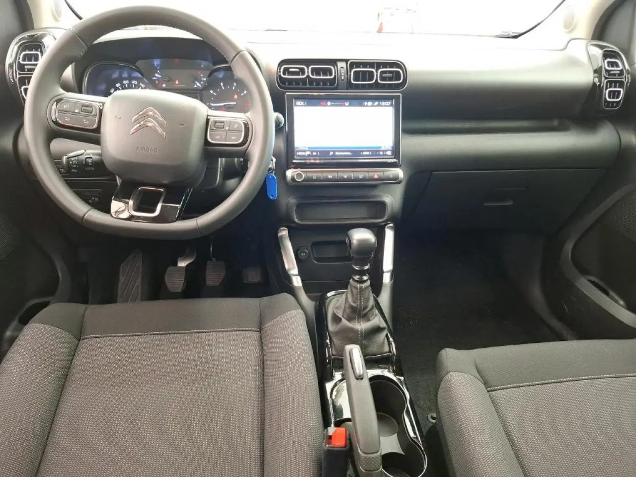 Vue intérieure avant du Citroën C3 Aircross 2023 avec tableau de bord noir, volant multifonction et console centrale brillante.