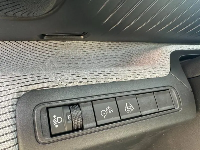 Gros plan sur les commandes situées côté gauche du tableau de bord, avec finition tissu gris et boutons de réglage lumineux et aides à la conduite.