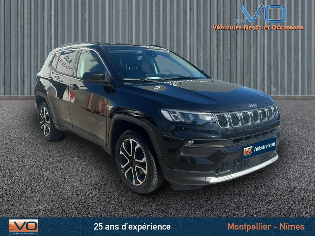 Jeep Compass noir en 3/4 avant droit, avec barres de toit et jantes 18 pouces visibles sur fond urbain.