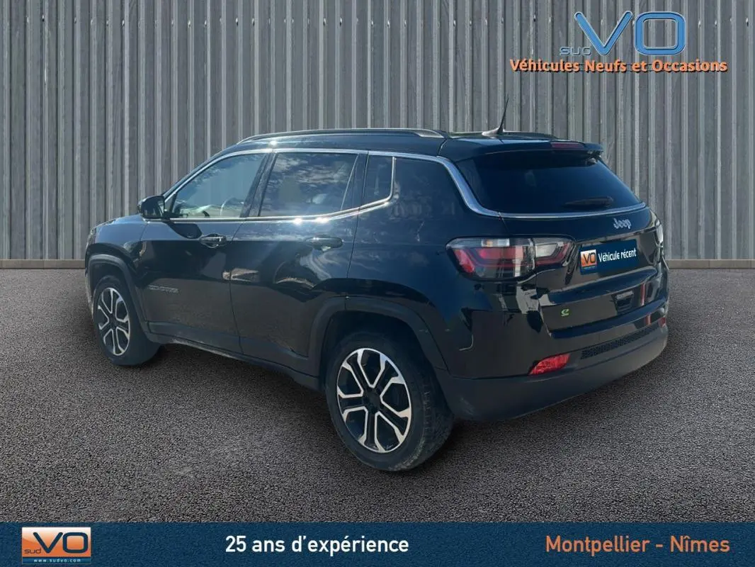 Jeep Compass noir en 3/4 arrière côté gauche, avec barres de toit et jantes 18 pouces visibles.