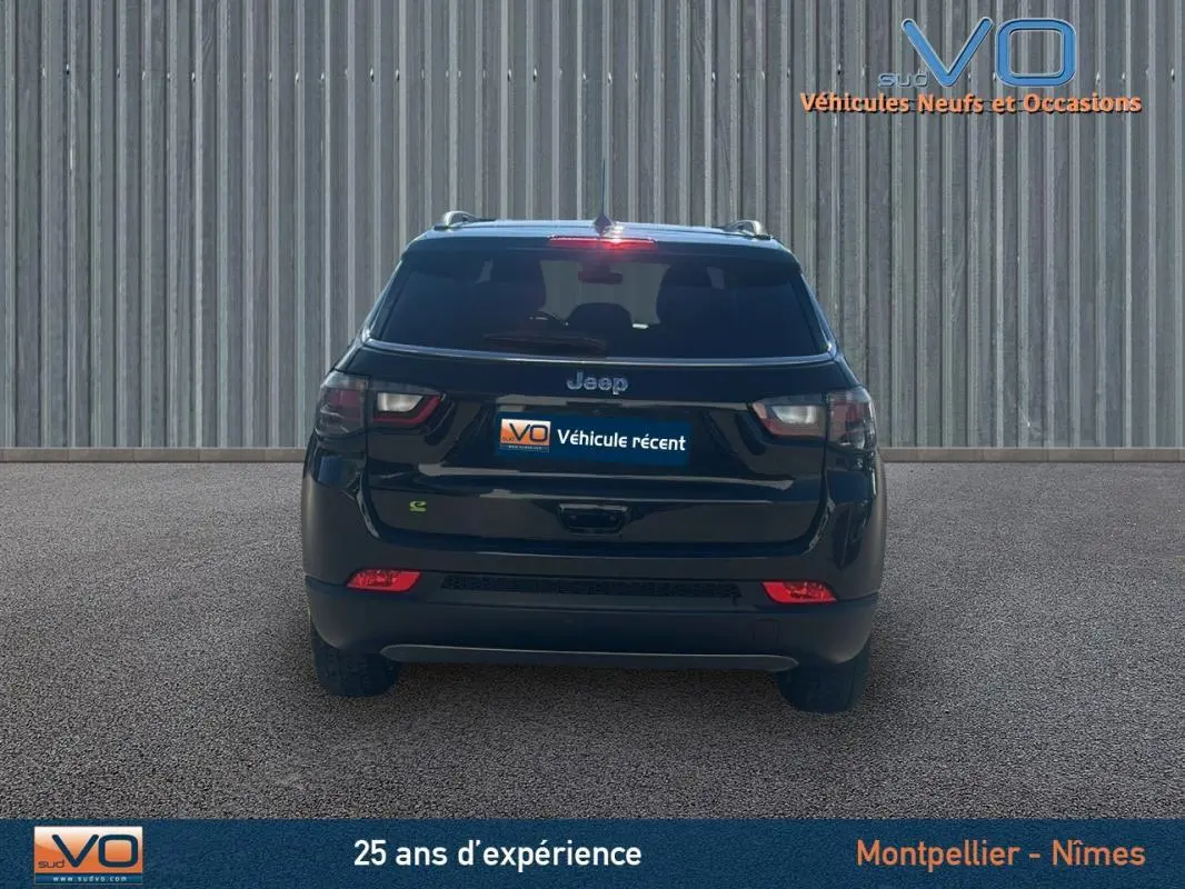 Vue arrière d'un Jeep Compass noir 2023 avec feux arrière LED et barres de toit visibles sur fond industriel.