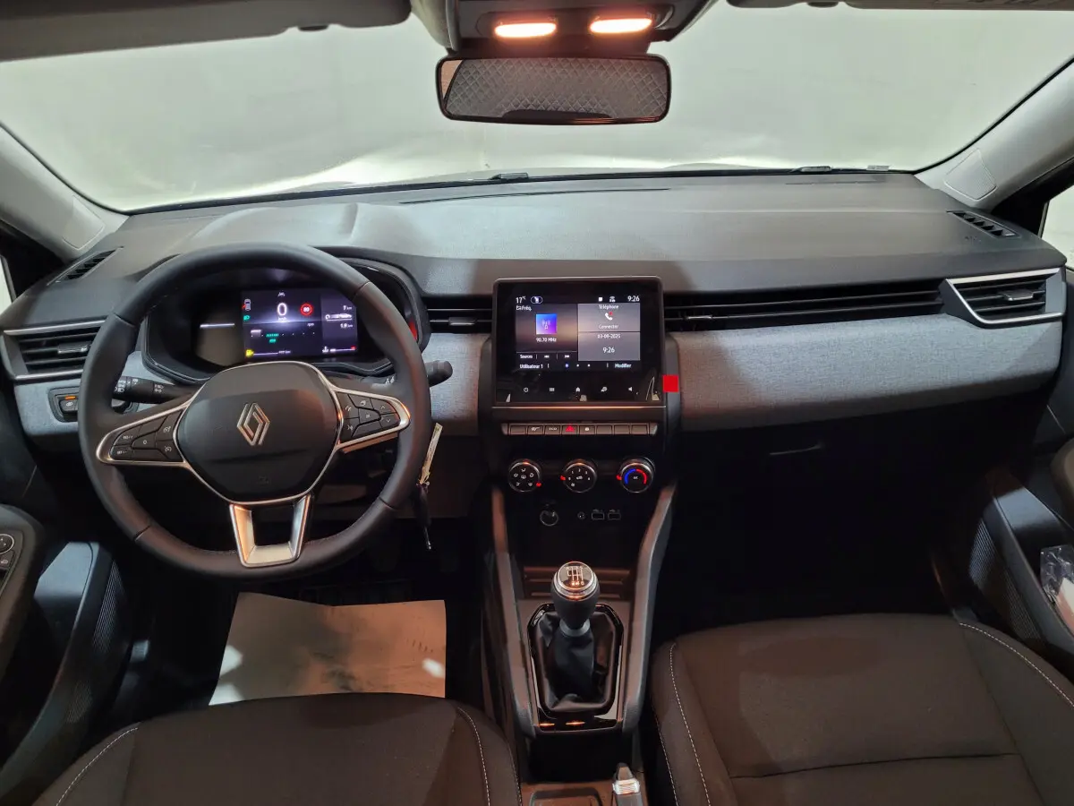 Intérieur de la Renault Clio 2025, vue frontale du tableau de bord avec écran tactile et volant multifonctions noir.