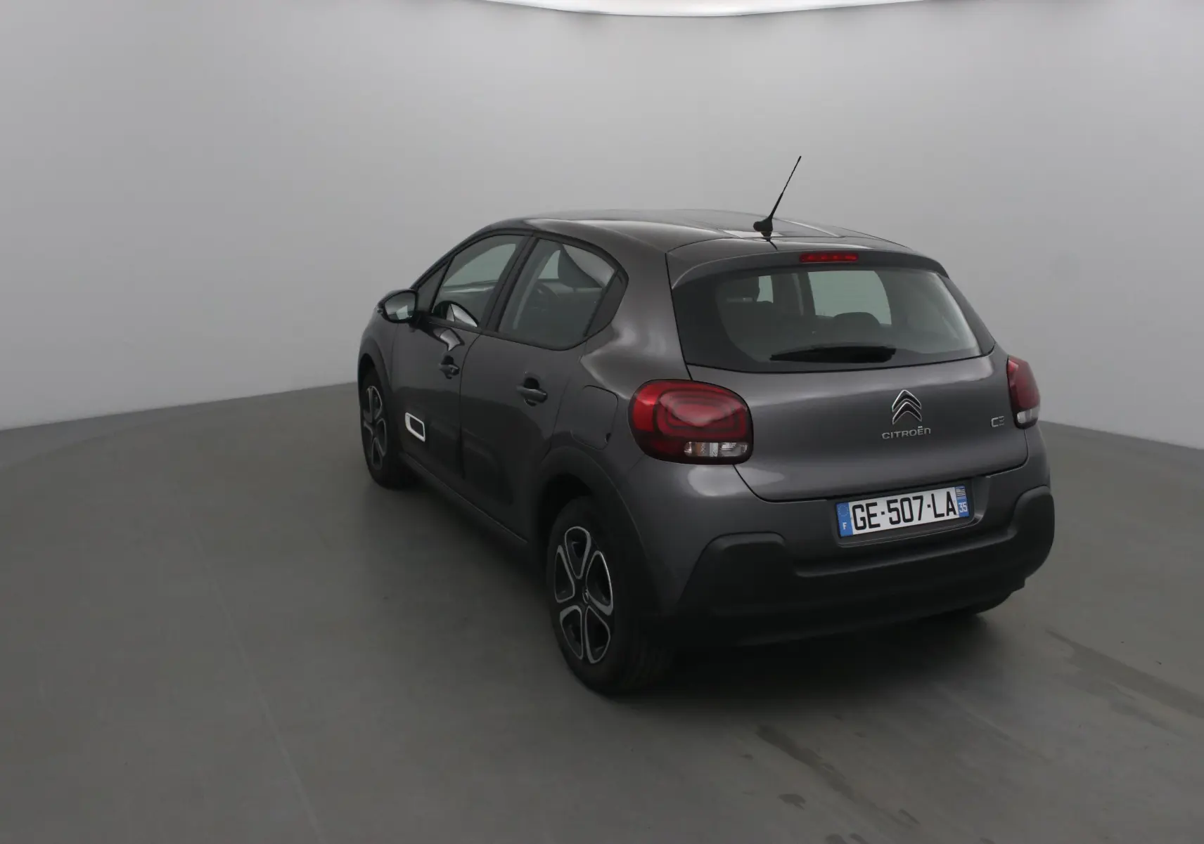 Vue 3/4 arrière gauche d'une Citroën C3 gris platinium 2022 avec feux arrière arrondis et jantes stylisées.