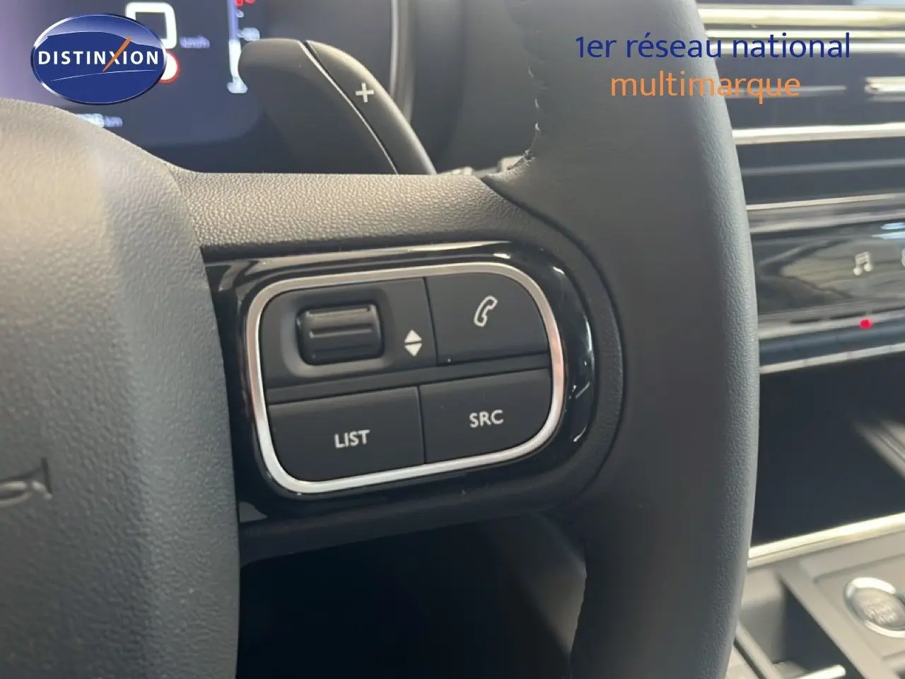 Gros plan sur les commandes au volant noir du Citroën C5 Aircross 2025 hybride, avec tableau de bord en arrière-plan.