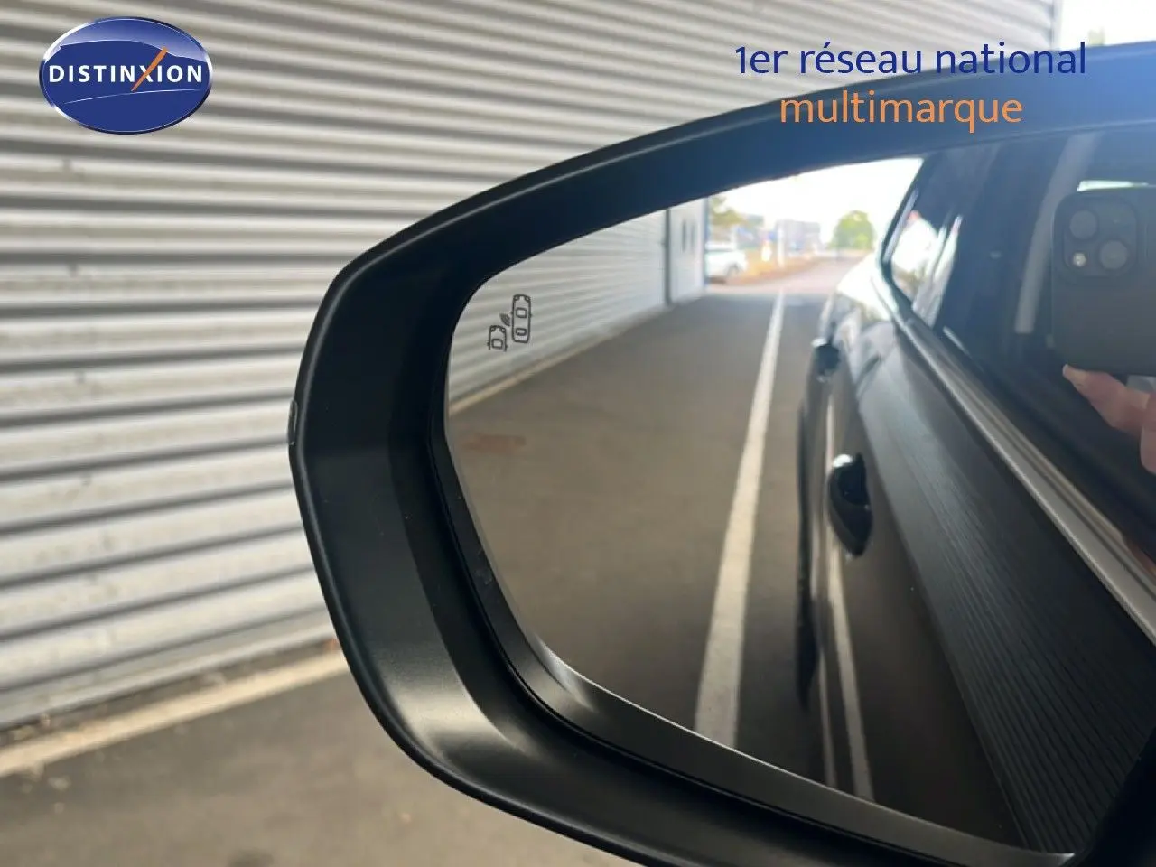 Rétroviseur côté droit d'une Citroën C5 Aircross noire métal 2025, avec reflet de la carrosserie et main tenant un téléphone.