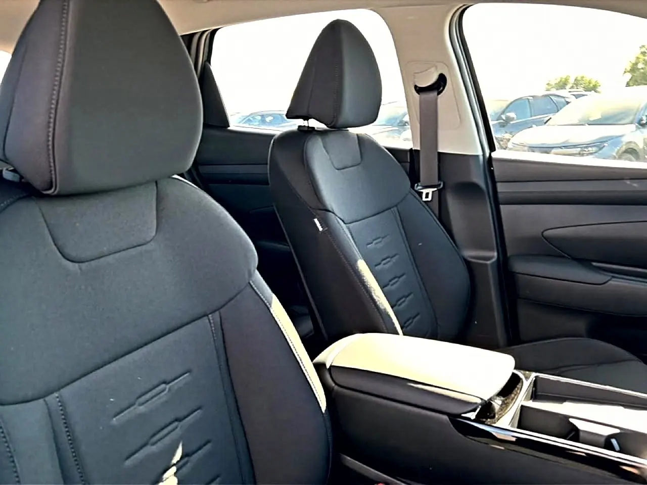 Vue intérieure côté droit des sièges avant noirs du Hyundai Tucson 2026 avec accoudoir central et ceinture de sécurité.