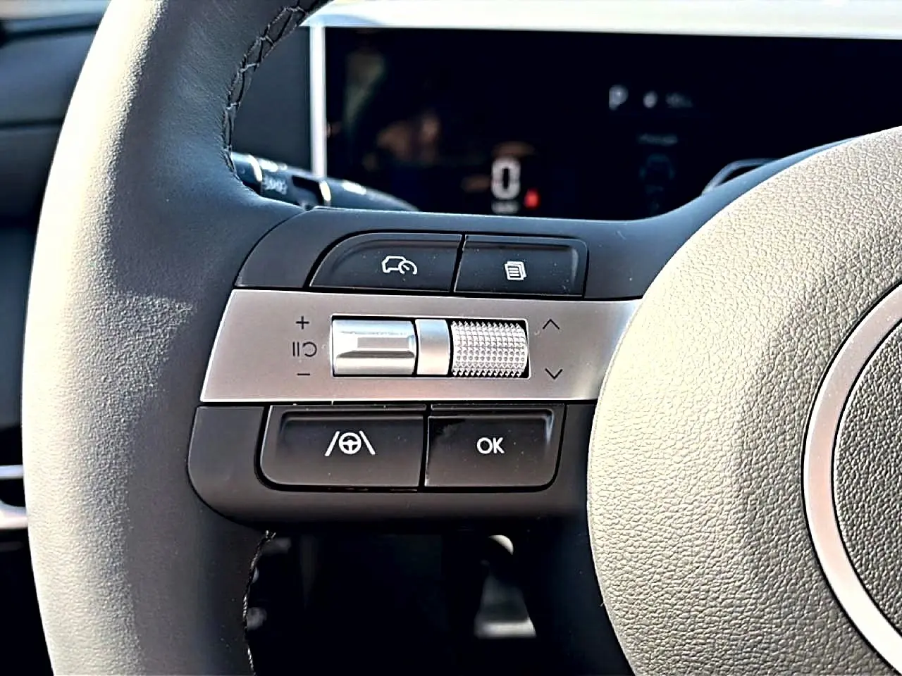 Gros plan sur les commandes gauche du volant cuir noir du Hyundai Tucson 2026 hybride, avec molette argentée.