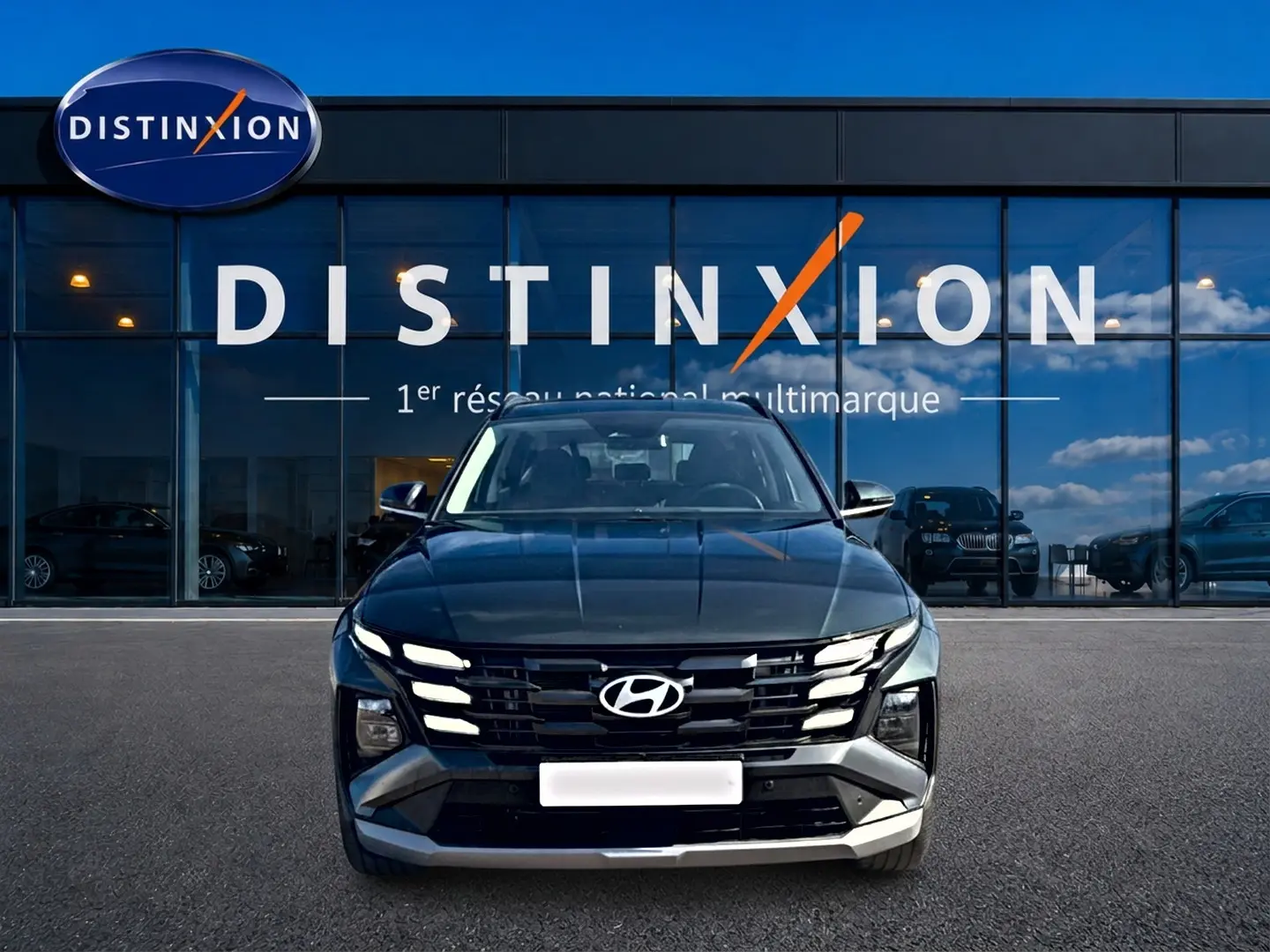 Vue avant d'un Hyundai Tucson vert 2026 avec calandre noire et feux LED distinctifs, devant une vitrine Distinxion.