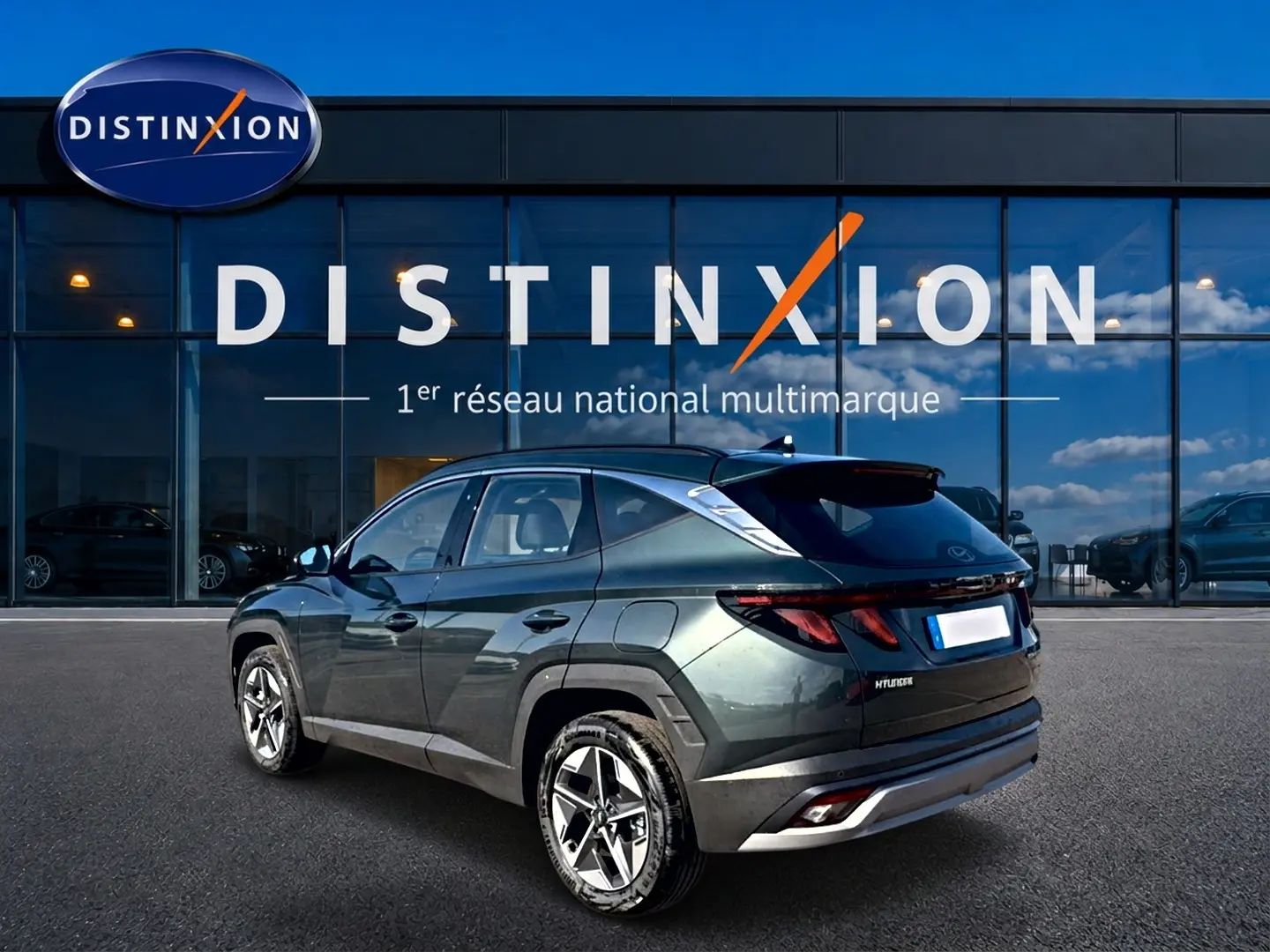 Vue 3/4 arrière gauche d'un Hyundai Tucson vert 2026 devant une vitrine Distinxion, jantes alu 18 pouces visibles.