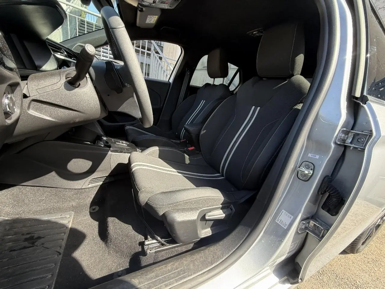 Vue intérieure côté conducteur de l’Opel Corsa 2025 gris graphite, montrant les sièges avant avec surpiqûres blanches et volant.