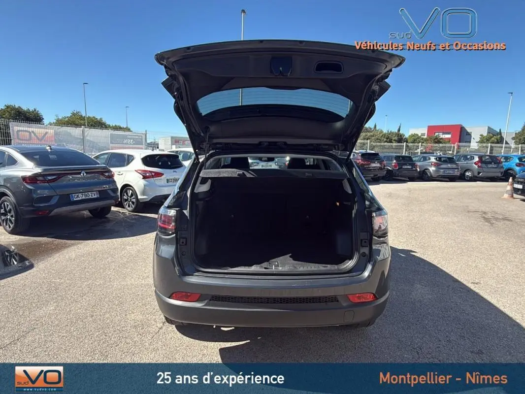 Vue arrière d'un Jeep Compass gris 2023 avec coffre ouvert, stationné en extérieur sous un ciel bleu.