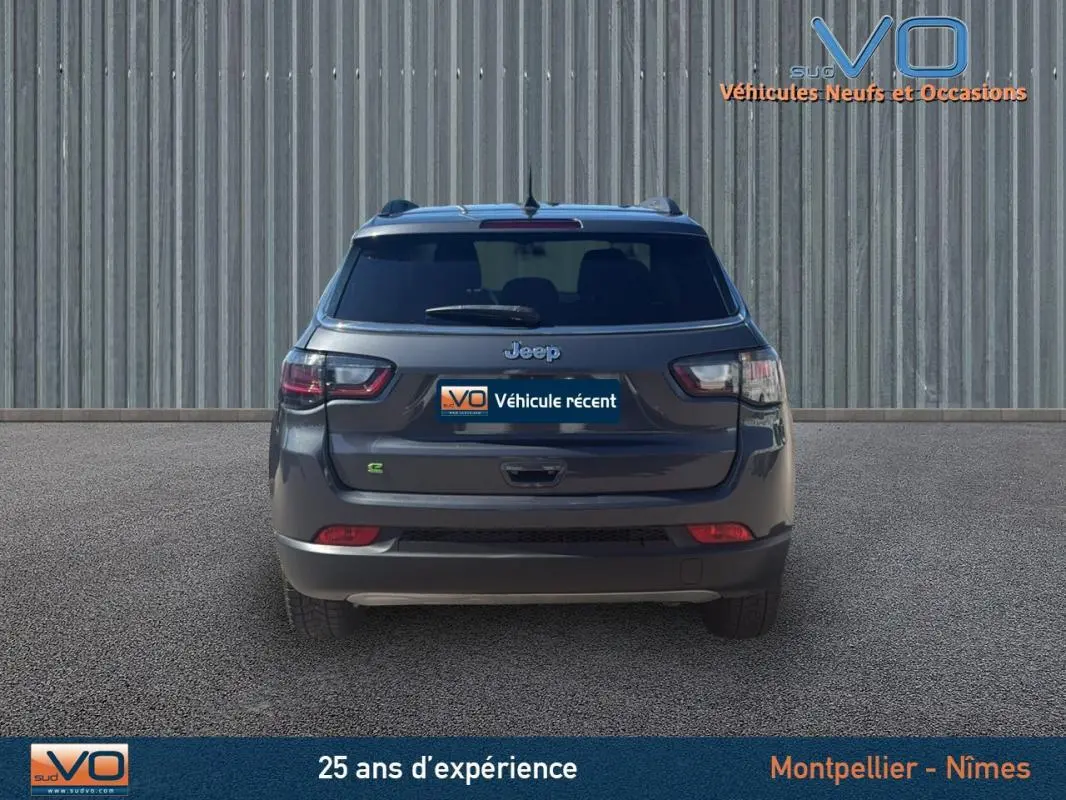 Vue arrière d'un Jeep Compass gris 2023 avec barres de toit et feux arrière LED visibles sur un sol goudronné.