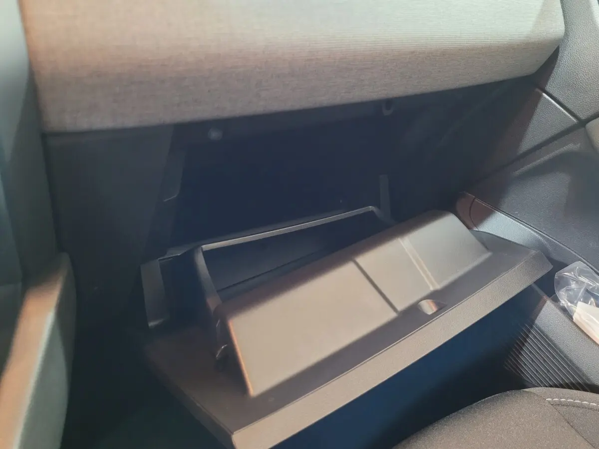 Gros plan sur la boîte à gants ouverte côté passager de la Renault Clio gris foncé, intérieur tissu clair et plastique noir.