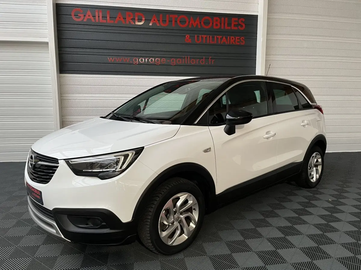 Opel Crossland X blanc vue 3/4 avant droit, toit noir et jantes alliage, stationné en intérieur showroom.
