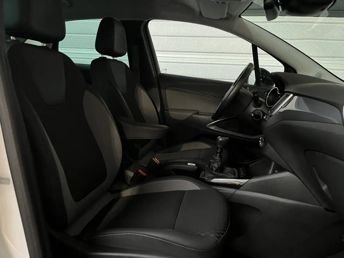 Vue intérieure côté conducteur de l'Opel Crossland X blanc, montrant les sièges noirs et la console centrale avec boîte manuelle.