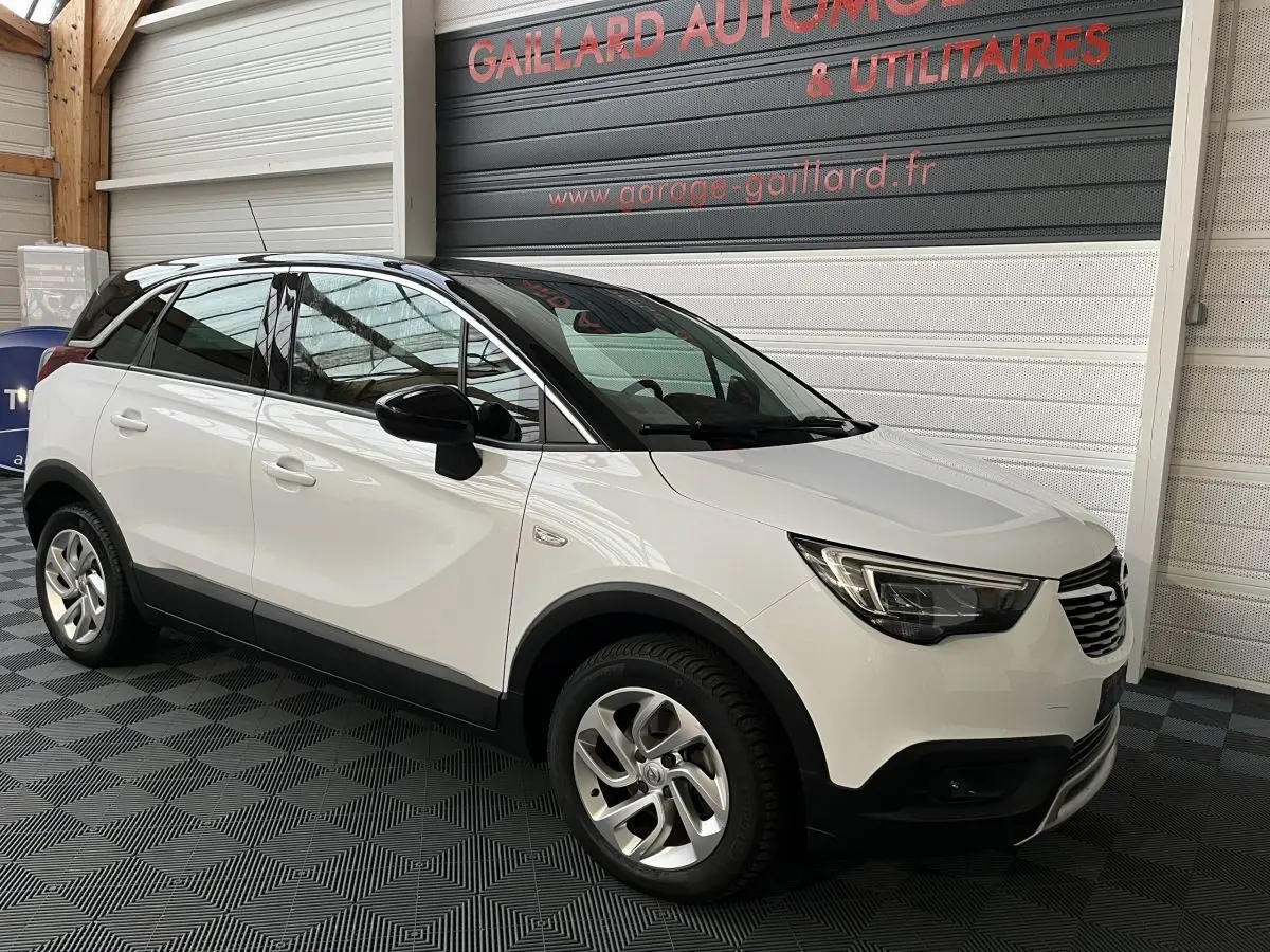 Vue 3/4 avant gauche d'un Opel Crossland X blanc avec toit noir, jantes alliage et détails noirs contrastants.