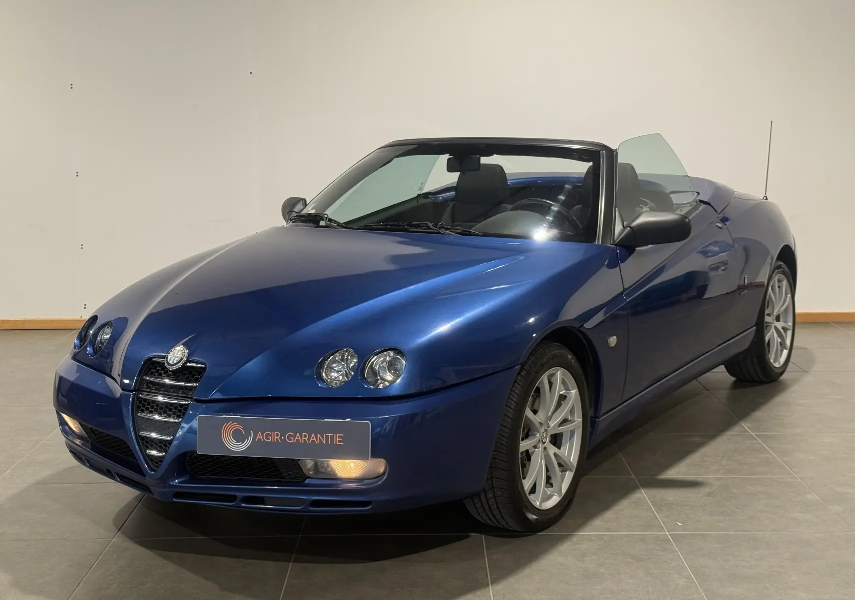 Vue 3/4 avant droite d'une Alfa Romeo Spider 2.0 JTS bleu cabriolet avec phares ronds et jantes argentées.