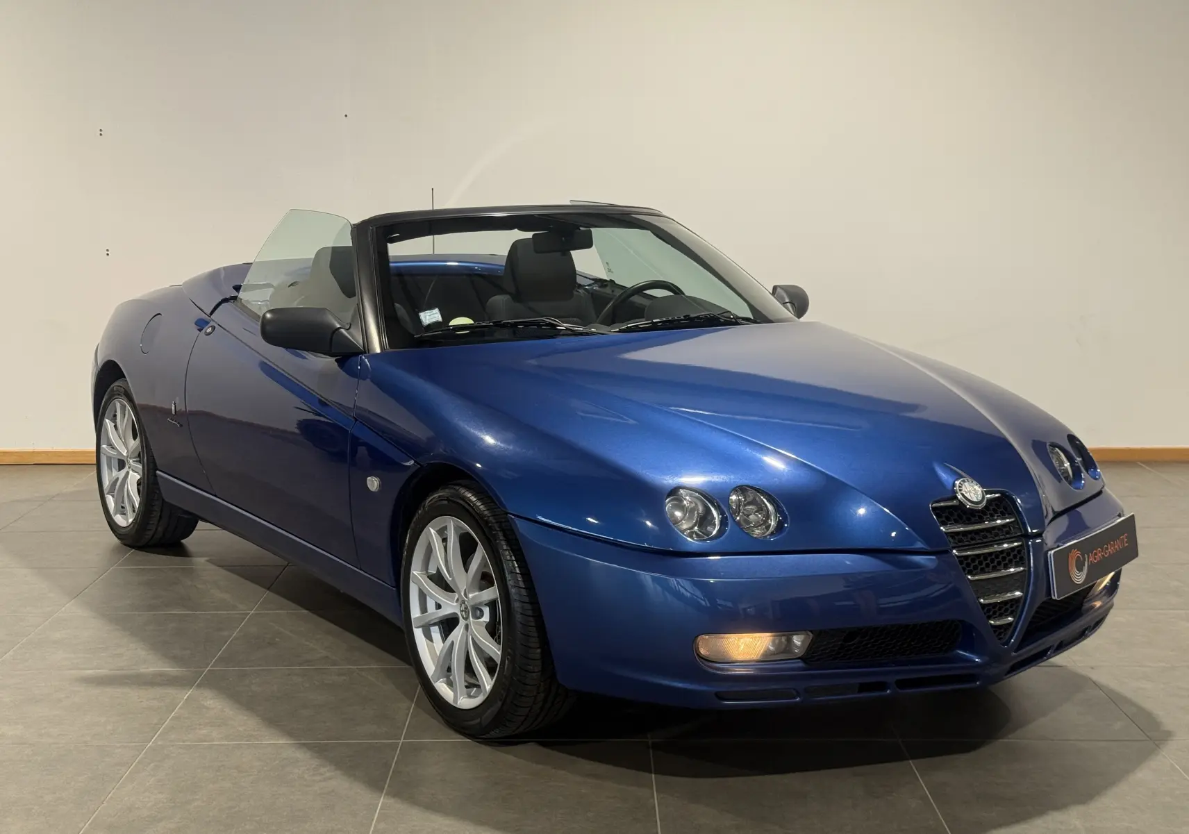 Alfa Romeo Spider 2.0 JTS bleu en cabriolet, vue 3/4 avant droit avec phares doubles caractéristiques.