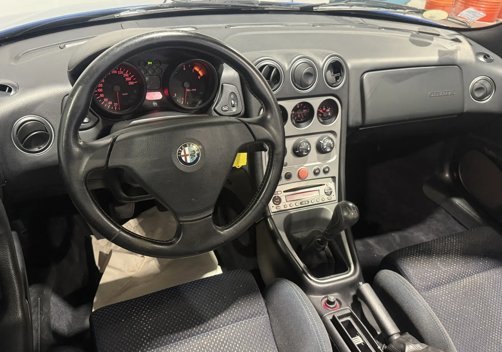 Vue intérieure de l'Alfa Romeo Spider 2.0 JTS 2006, volant cuir, tableau de bord noir et levier de vitesse manuel.