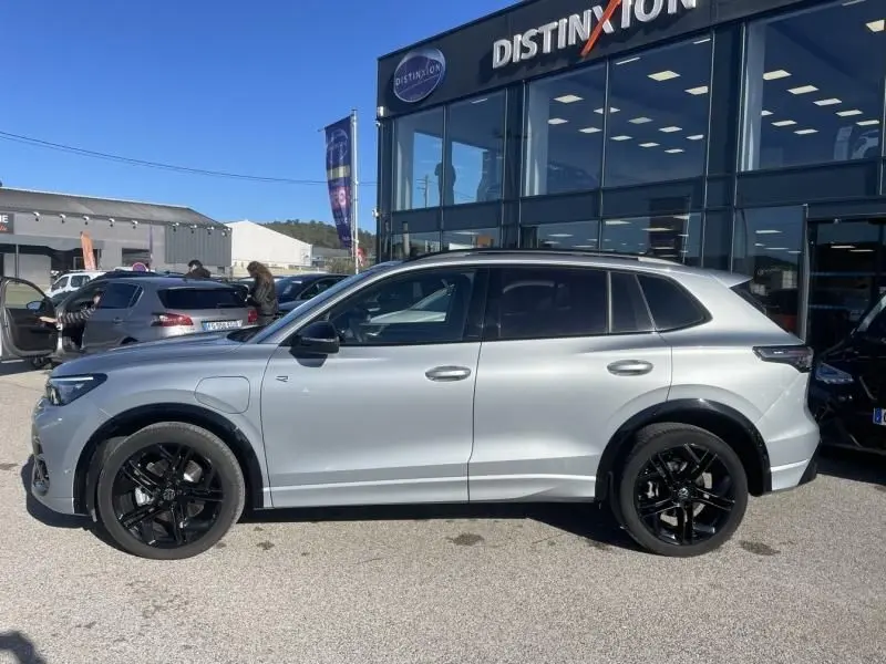 Vue de profil côté gauche d'un Volkswagen Tiguan 1.5 eHybrid gris métal avec jantes noires, devant un showroom.