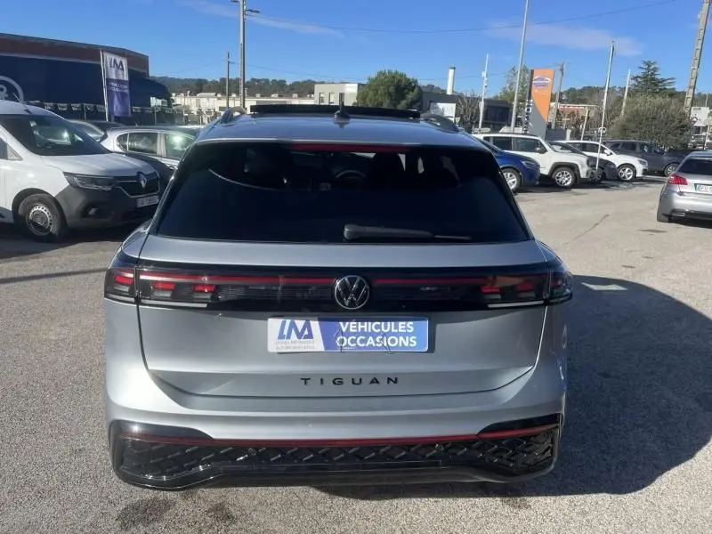 Vue arrière d'un Volkswagen Tiguan gris métal 2025 avec bande lumineuse et logo VW au centre, en extérieur.