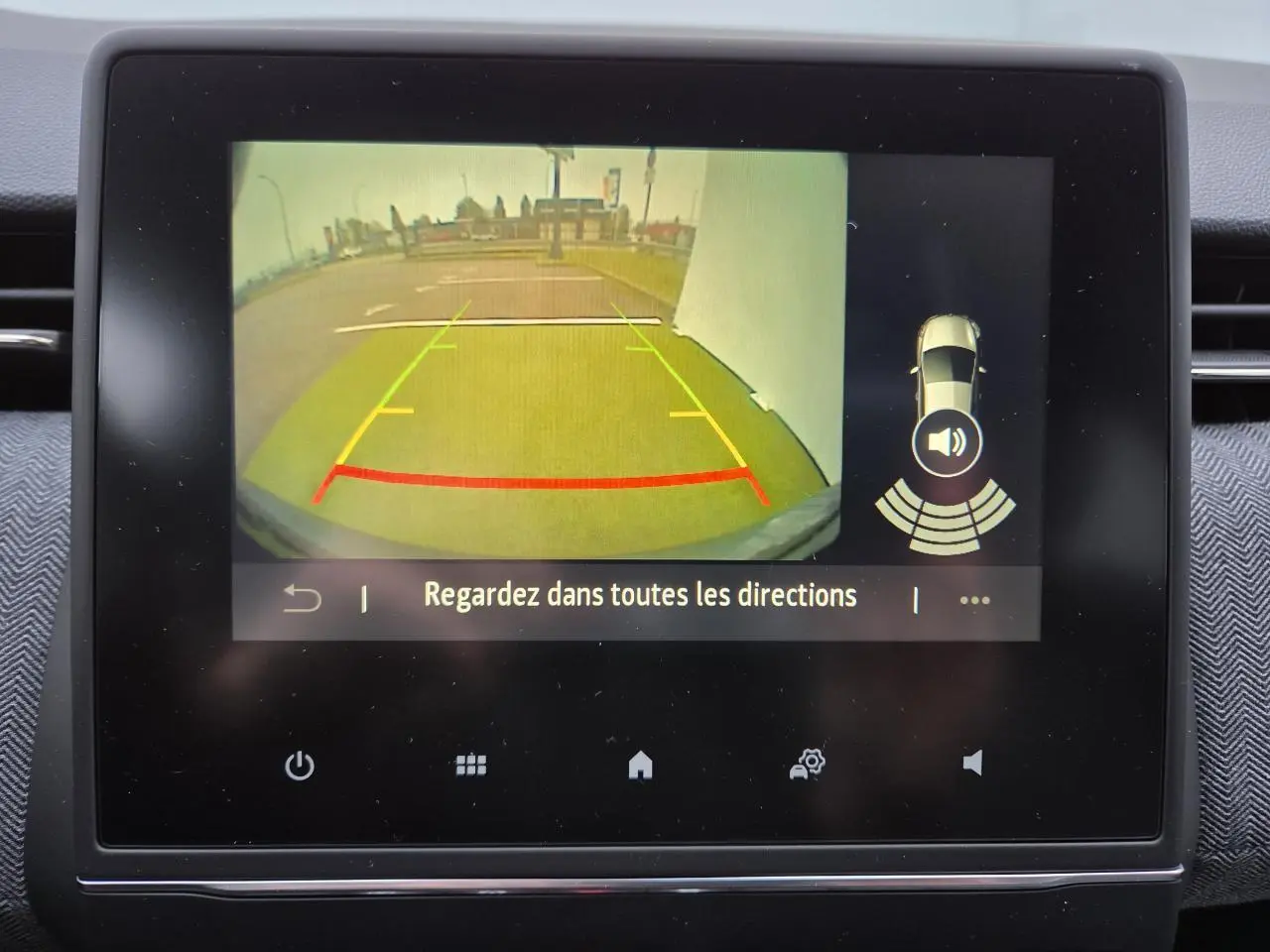 Écran multimédia montrant la caméra de recul de la Renault Clio gris schiste, avec guidage de trajectoire coloré.