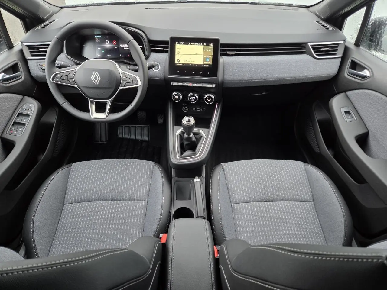 Vue intérieure avant de la Renault Clio 2025, tableau de bord gris mélangé avec volant multifonction et boîte manuelle.