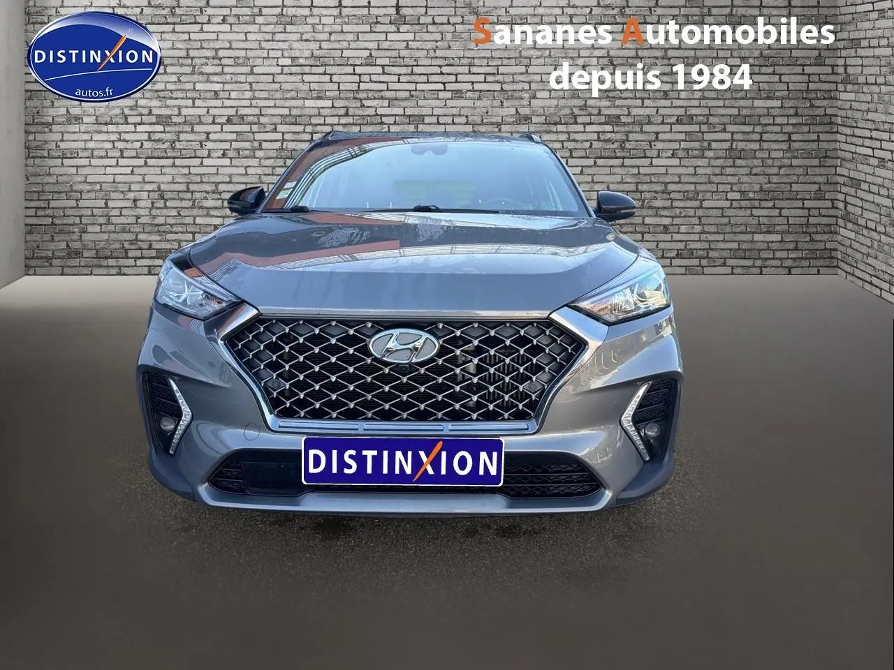 Vue frontale d'un Hyundai Tucson 1.6 Hybrid gris foncé avec calandre large et phares LED distinctifs.