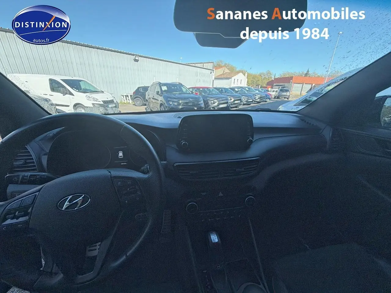 Vue intérieure du tableau de bord et volant du Hyundai Tucson gris foncé, avec écran tactile central et commandes au volant visibles.