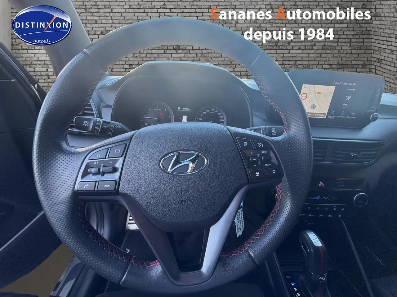 Vue intérieure centrée sur le volant cuir N Line avec surpiqûres rouges et écran tactile du Hyundai Tucson gris foncé.