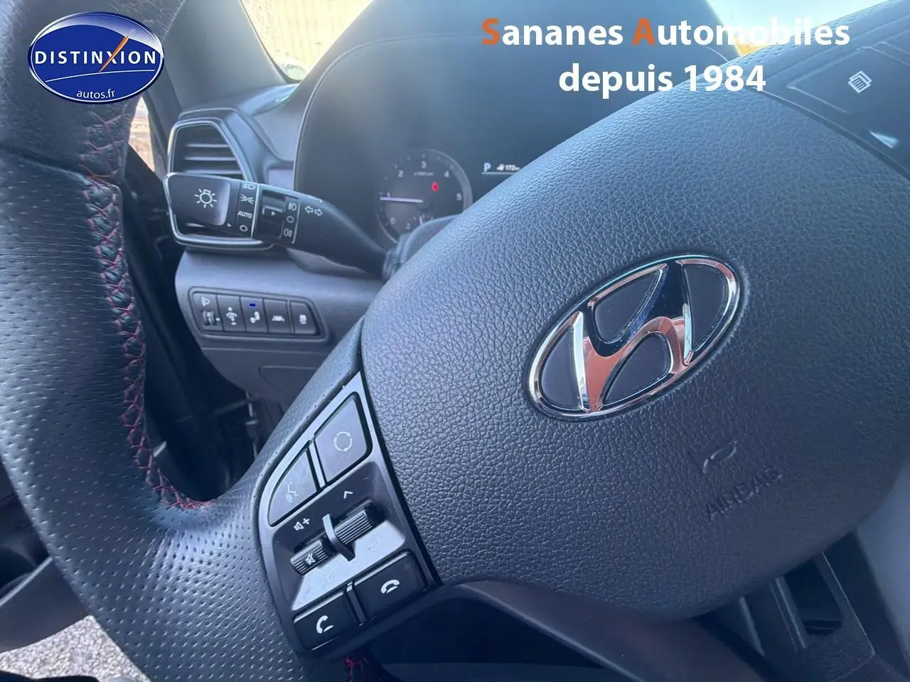 Gros plan sur le volant cuir perforé avec surpiqûres rouges du Hyundai Tucson 1.6 Hybrid gris foncé, tableau de bord partiel visible.