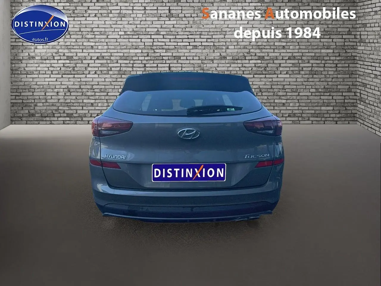 Vue arrière d'un Hyundai Tucson gris foncé 2020, avec logo et feux arrière visibles sur fond de mur en briques.