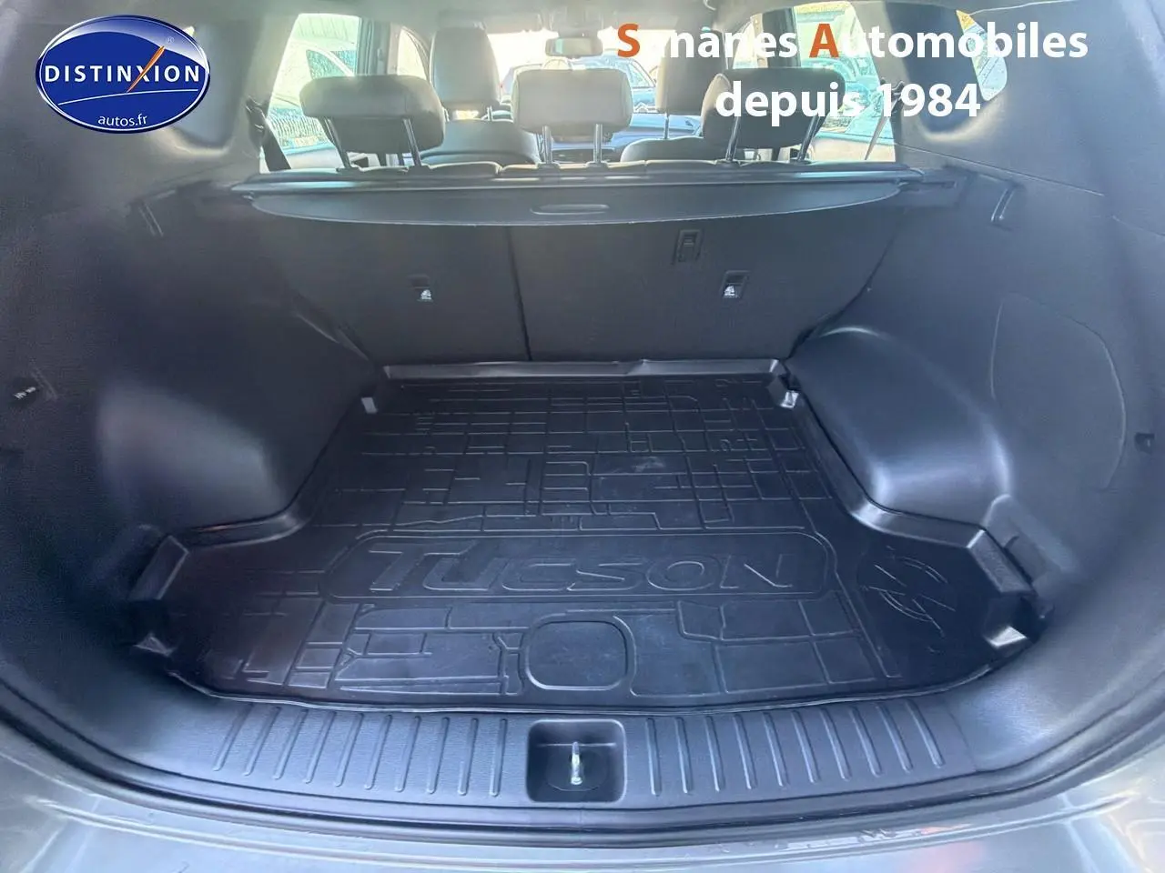 Coffre ouvert du Hyundai Tucson gris foncé, vue arrière montrant le tapis de coffre avec inscription Tucson.