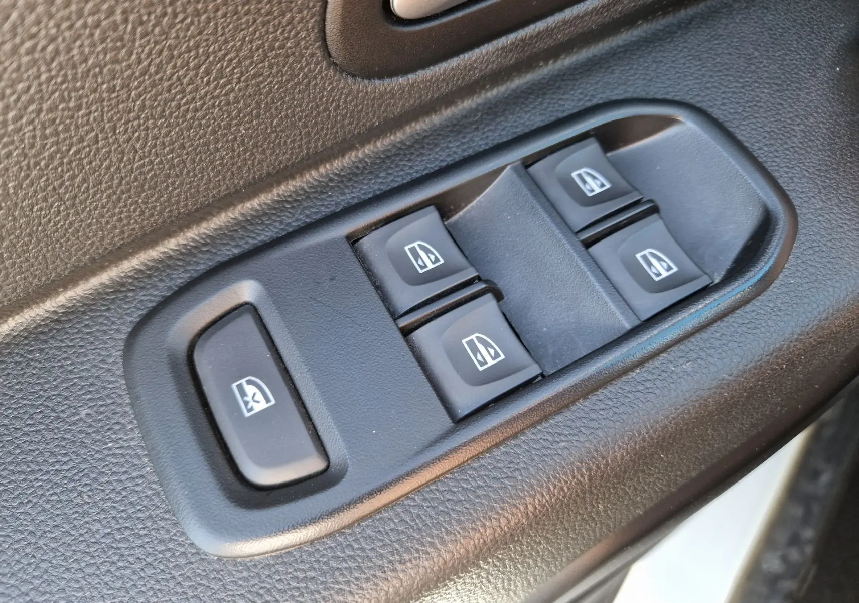 Gros plan sur les commandes électriques des vitres côté conducteur du Dacia Duster blanc 2024.