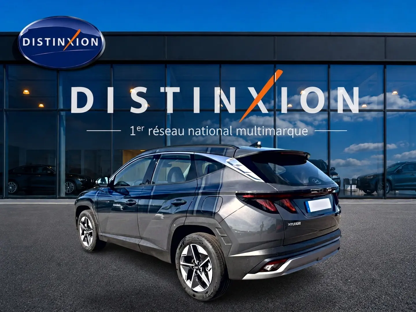 Hyundai Tucson 1.6 t-gdi 239 hybride gris ecotronic, vue 3/4 arrière droit devant un showroom Distinxion.