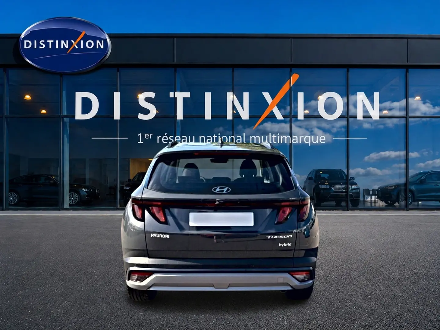 Vue arrière d'un Hyundai Tucson gris ecotronic 2026 hybride garé devant une vitrine avec logo Distinxion.