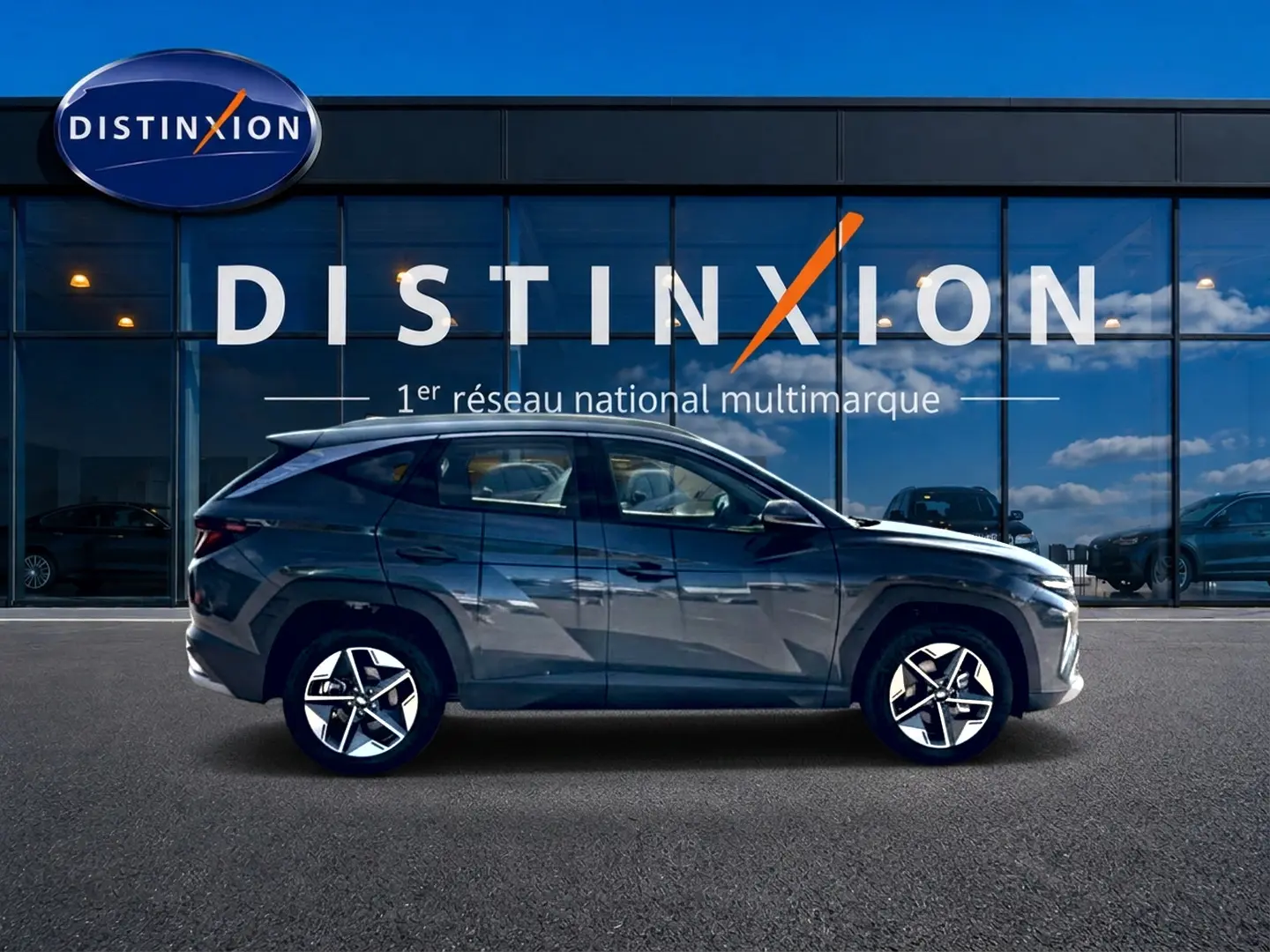 Vue de profil côté gauche d'un Hyundai Tucson gris ecotronic garé devant une vitrine avec logo Distinxion.