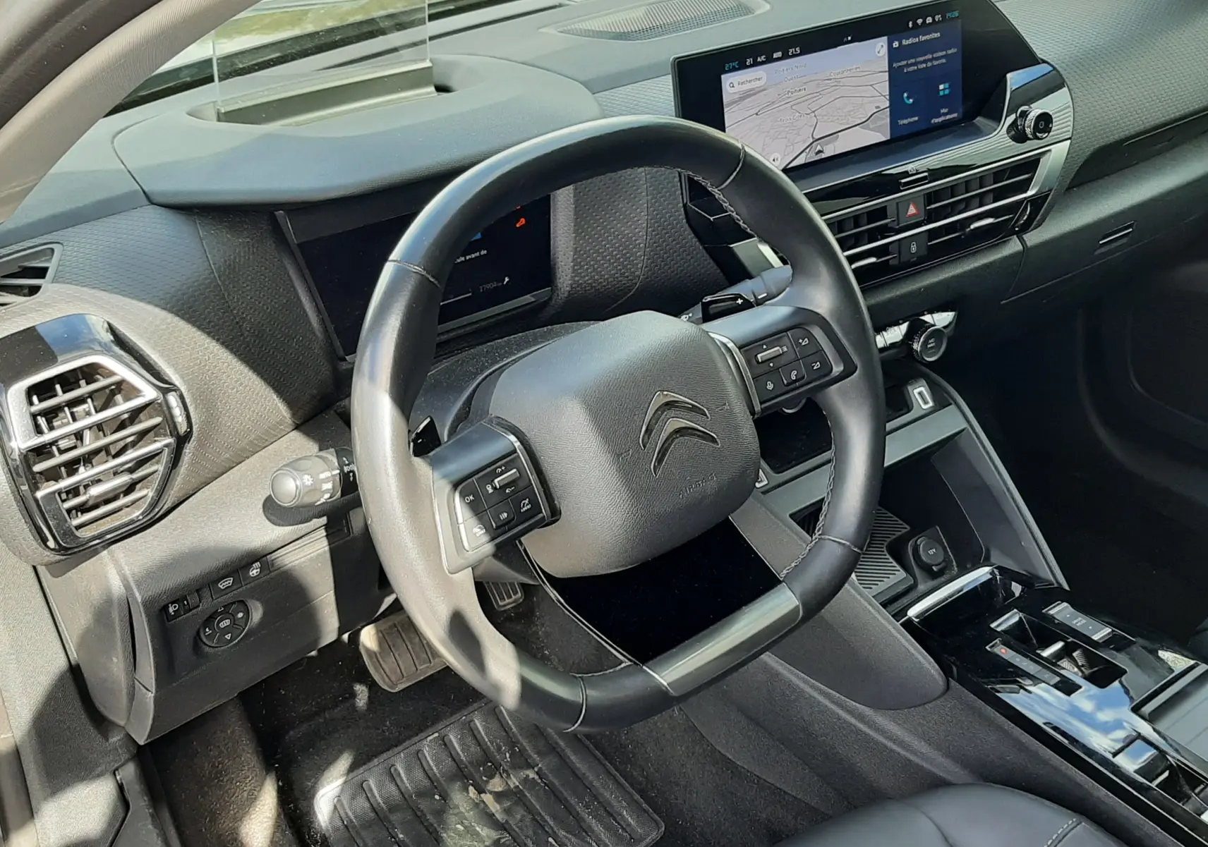 Vue intérieure côté conducteur du tableau de bord gris et noir de la Citroën C4 1.2 PureTech 2024 avec écran tactile et volant multifonction.