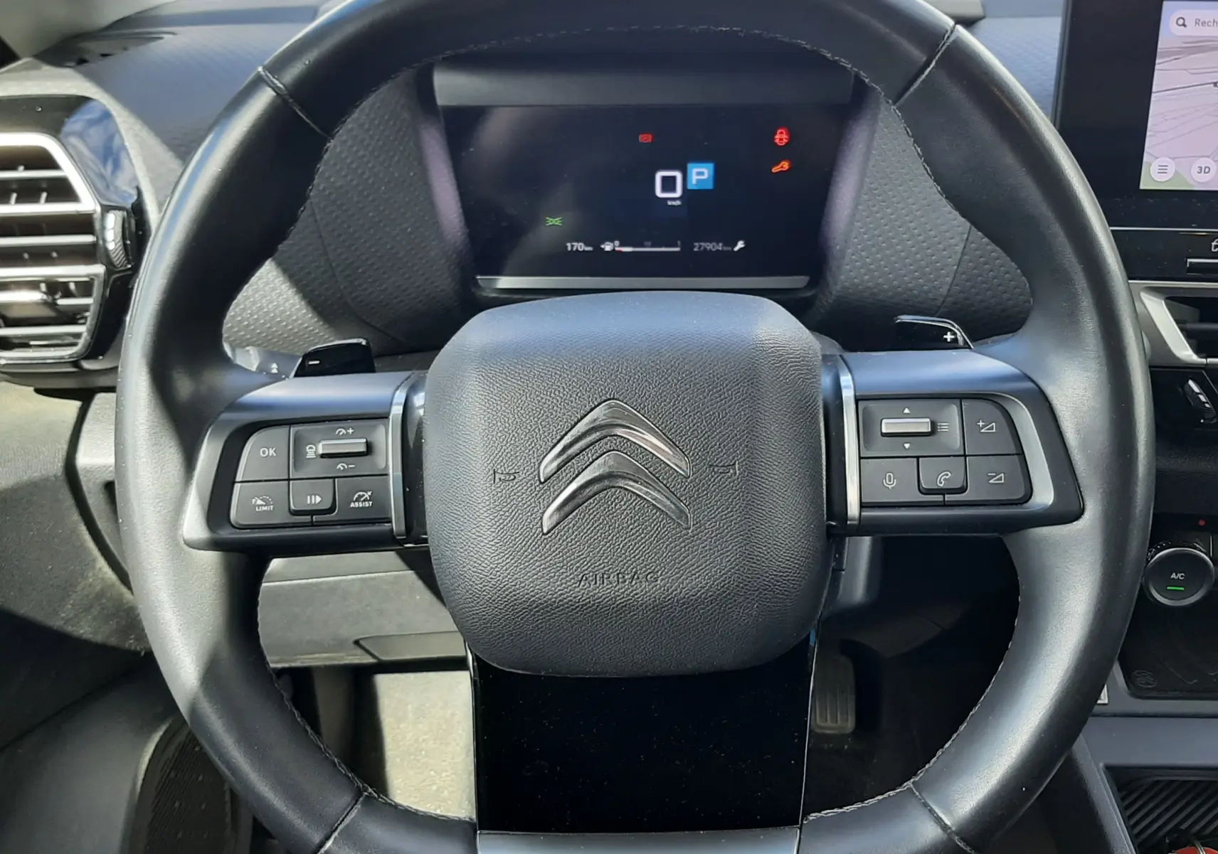 Vue rapprochée du volant noir de la Citroën C4 2024 avec commandes intégrées et tableau de bord numérique en arrière-plan.
