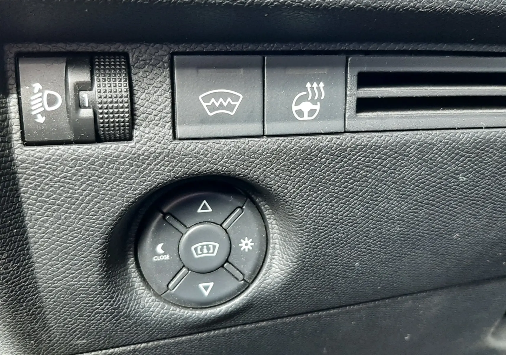 Gros plan sur les commandes noires de réglage des phares, dégivrage et volant chauffant du tableau de bord d'une Citroën C4 gris 2024.