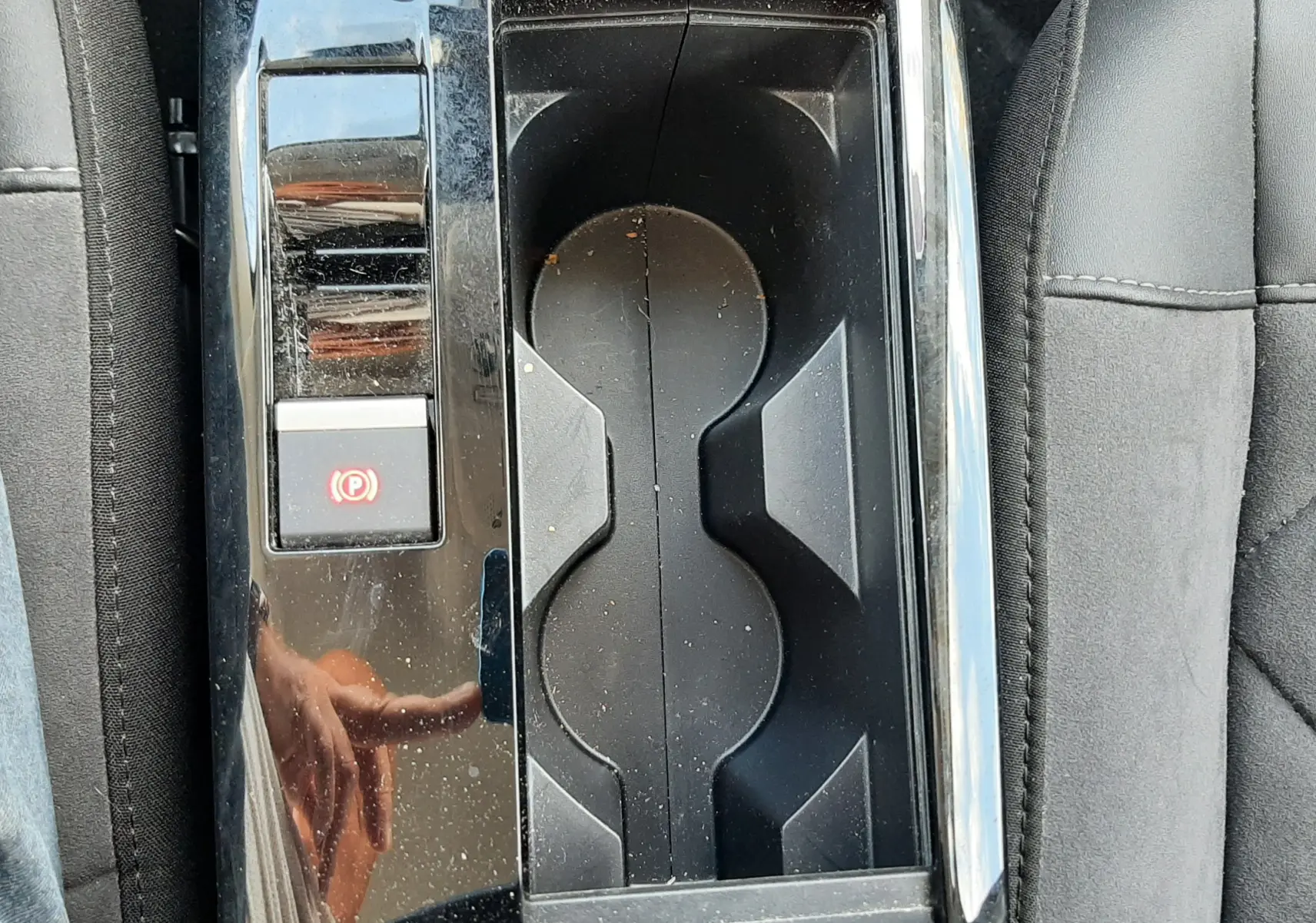 Gros plan sur la console centrale noire brillante avec porte-gobelets et bouton de frein à main électrique dans une Citroën C4 gris.