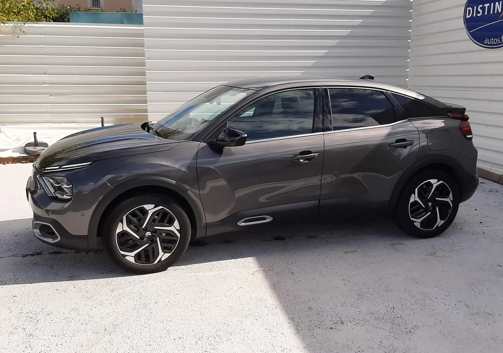 Profil côté gauche d'une Citroën C4 gris 2024, avec jantes bi-ton et vitres teintées, sur fond urbain clair.