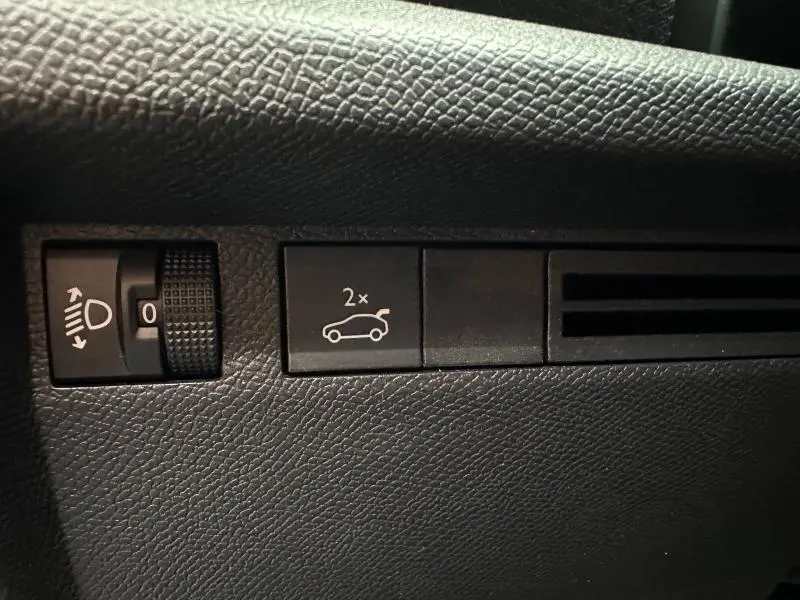 Gros plan sur les commandes intérieures noires du tableau de bord d'une Citroën C4 X 2025, avec bouton d'ouverture du coffre.