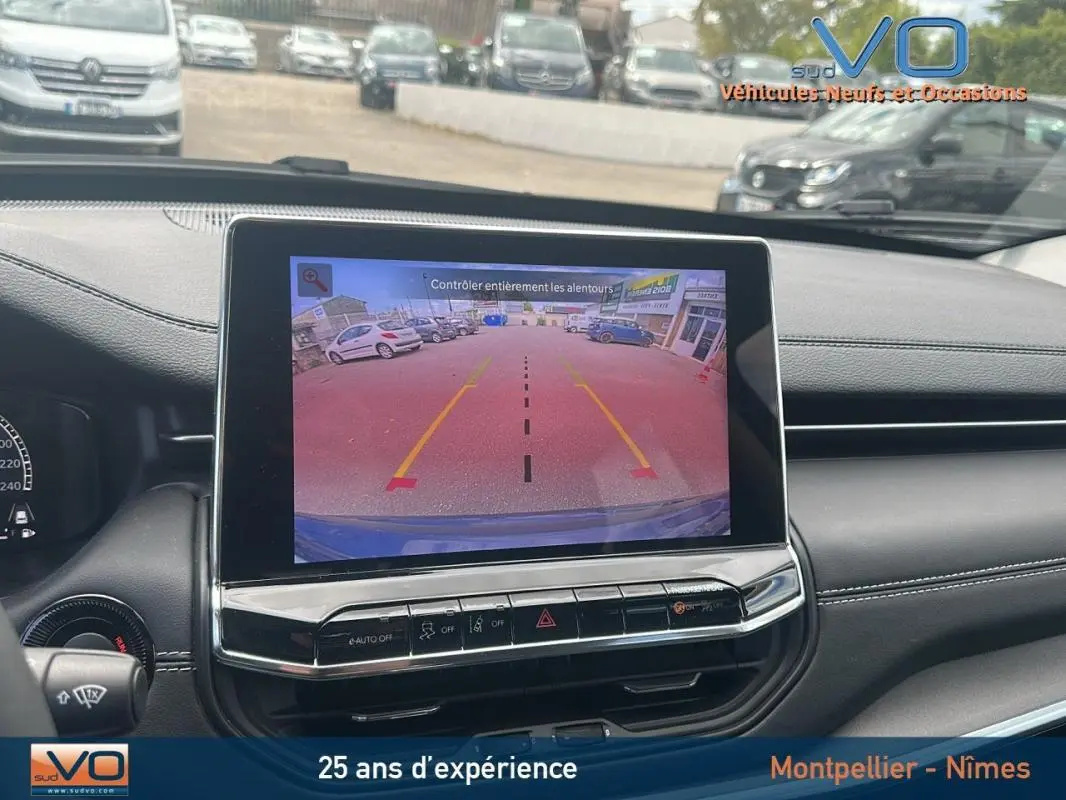 Vue intérieure du tableau de bord du Jeep Compass bleu 2023 avec écran tactile affichant la caméra de recul et commandes intégrées.